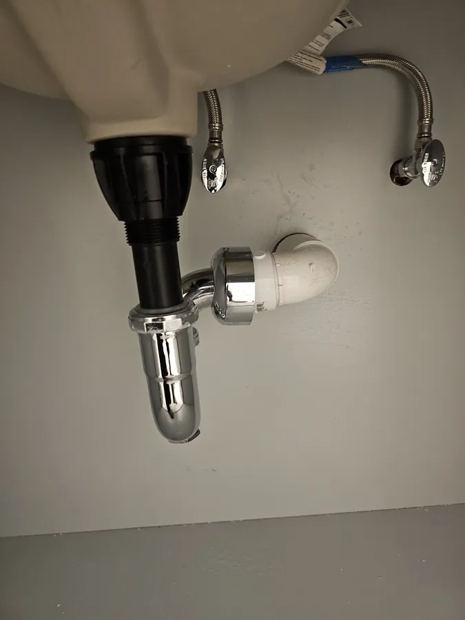 New braided supply lines and a chrome P-trap under a bathroom sink